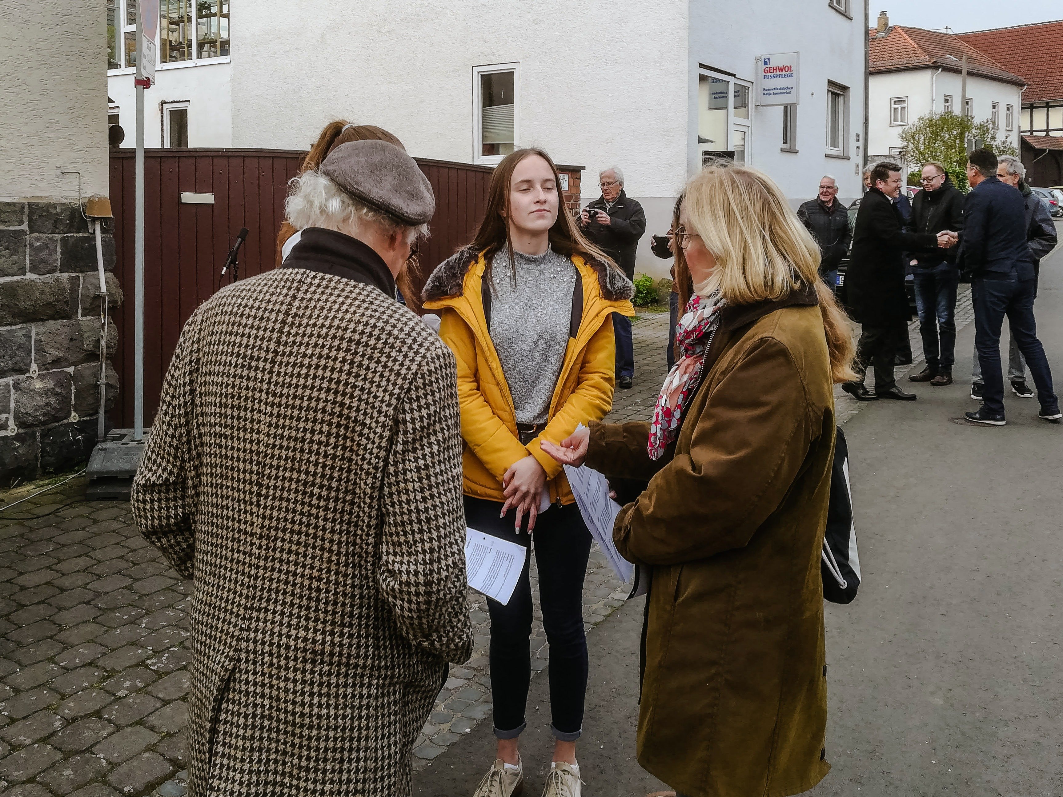 Drei Menschen im Gespräch auf der Straße, dahinter weitere Gäste