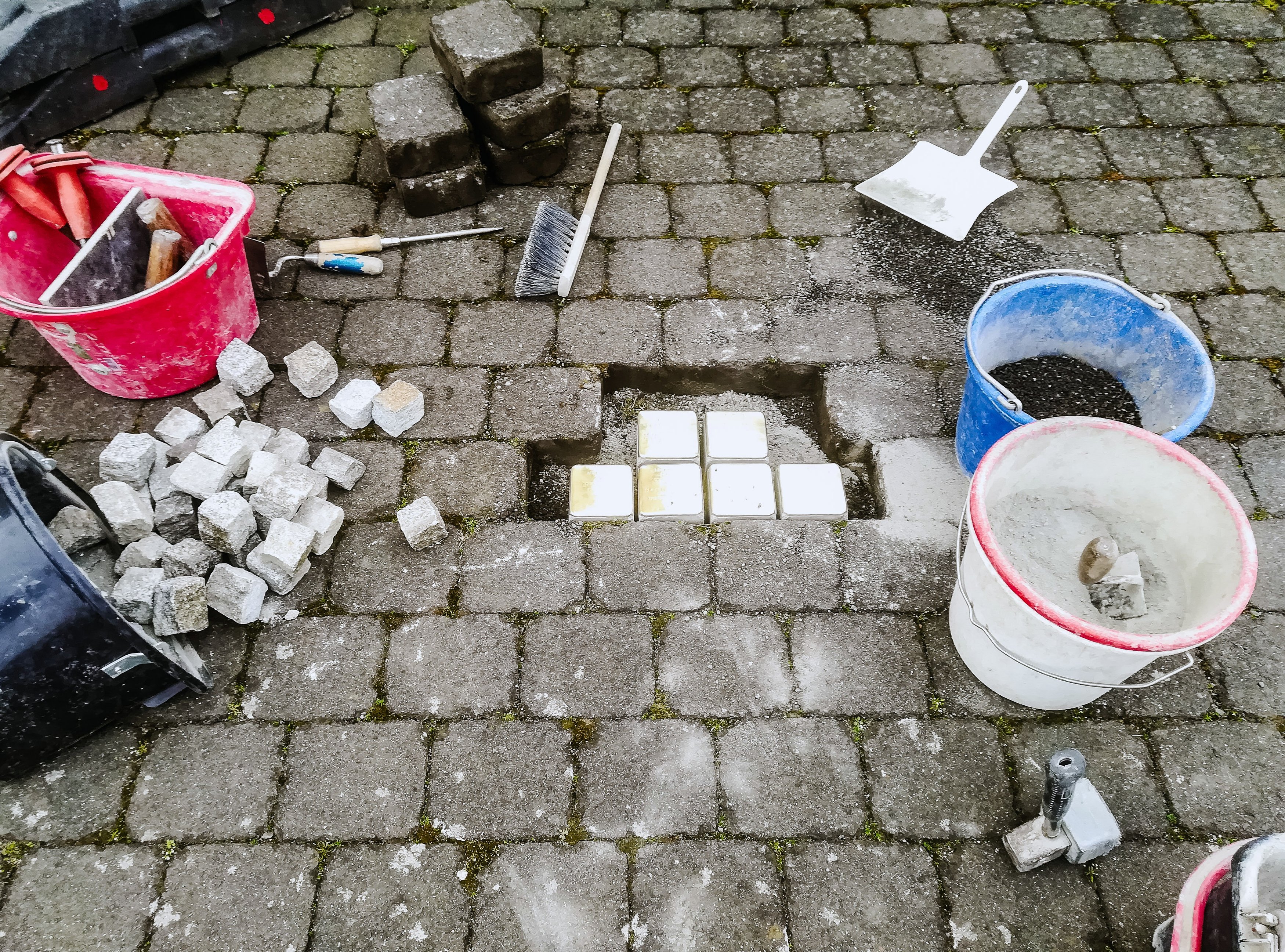 Sechs neue Stolpersteine im Pflaster, ringsum Werkzeug, Eimer und Pflastersteine