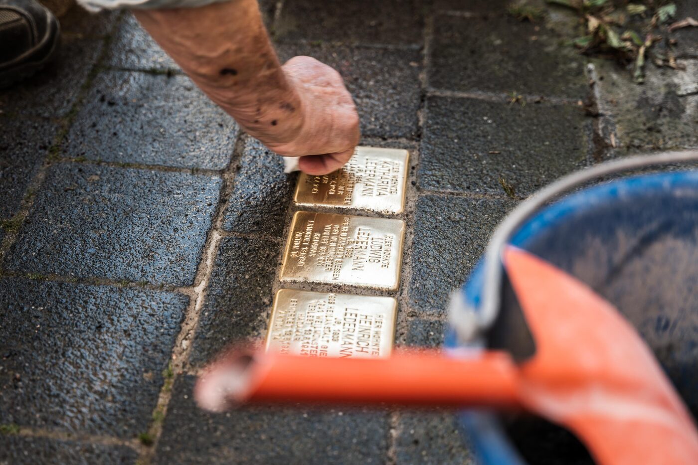 Eine Hand rückt einen von drei Stolpersteinen im Pflaster zurecht.