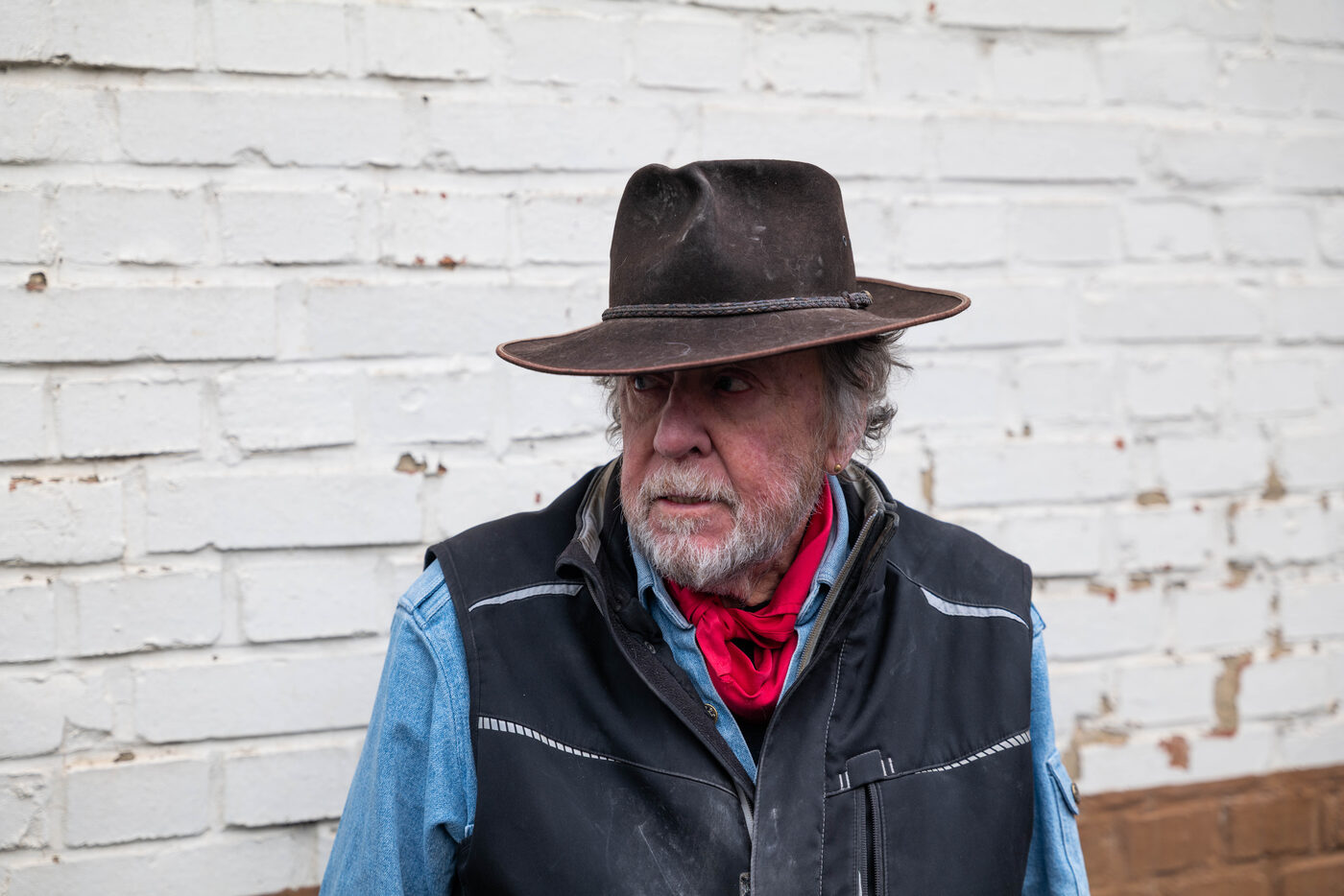Gunter Demnig mit Hut und rotem Halstuch vor einer weißen Wand.