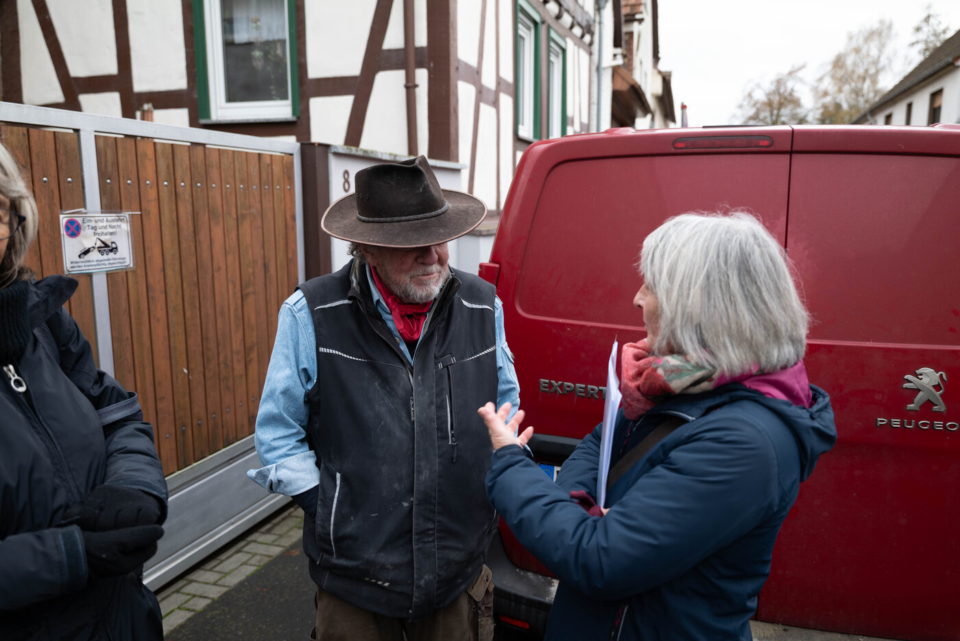 Gunter Demnig und eine Frau mit Papieren im Gespräch vor einem roten Transporter.