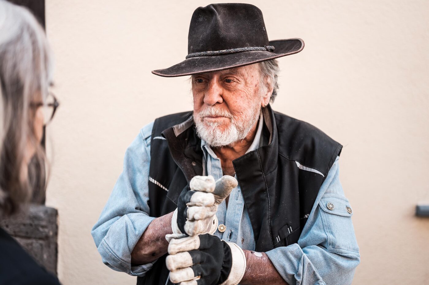 Gunter Demnig mit Hut und Arbeitshandschuhen vor einer hellen Hauswand.