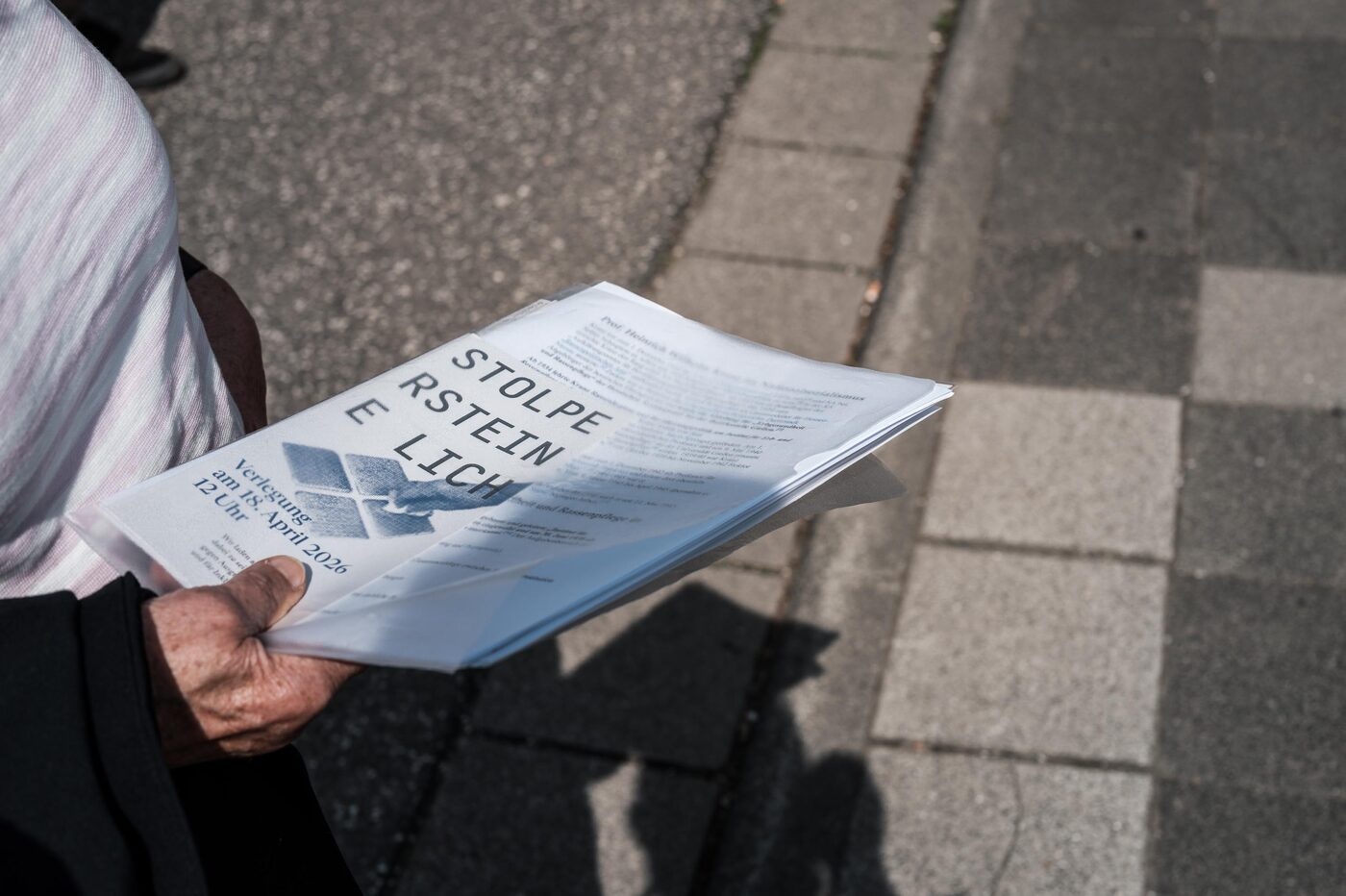 Eine Hand hält das gefaltete Programmblatt mit der Aufschrift „Stolpersteine Lich“.
